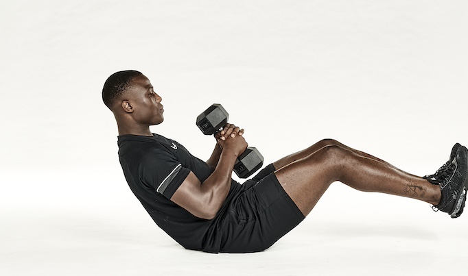 Man in black shorts and black training top performing dumbbell Russian twist