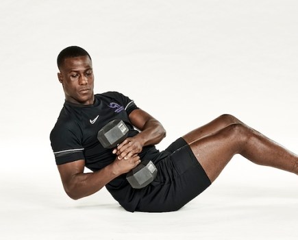 Man in black shorts and black training top performing dumbbell Russian twist
