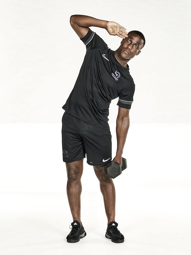 Man in black shorts and black training top performing dumbbell side crunch