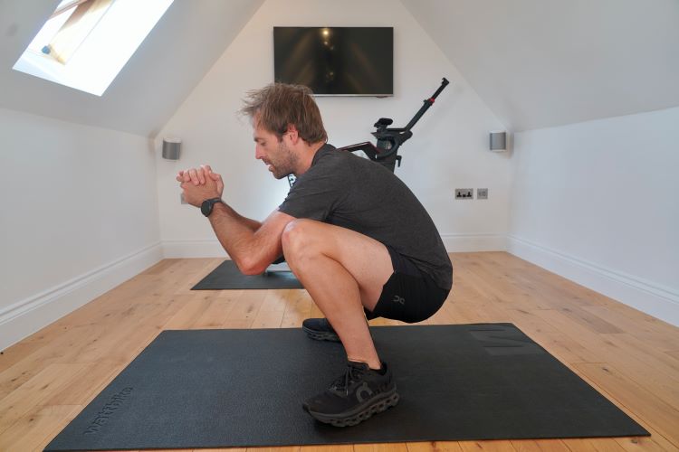 Man performing a deep yoga squat in a home gym