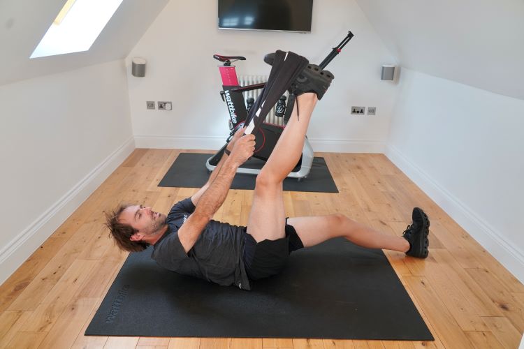 Man lying down performing a dynamic hamstring stretch, One of the best strength exercises for cyclists