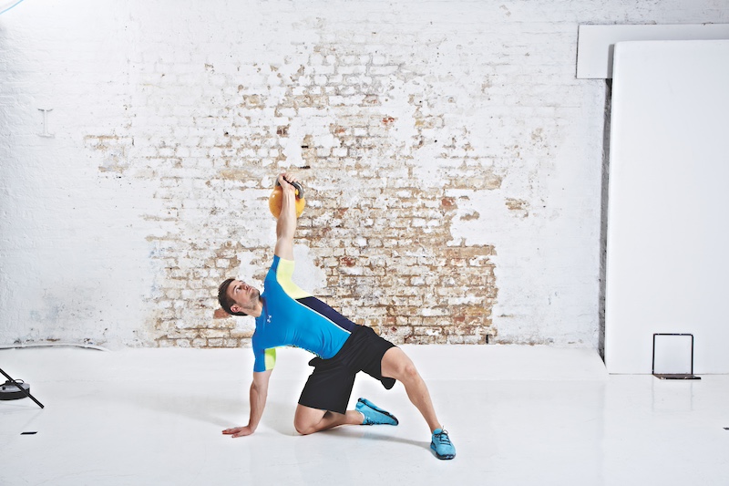 Man in blue top and black shorts performing kettlebell Turkish get-up