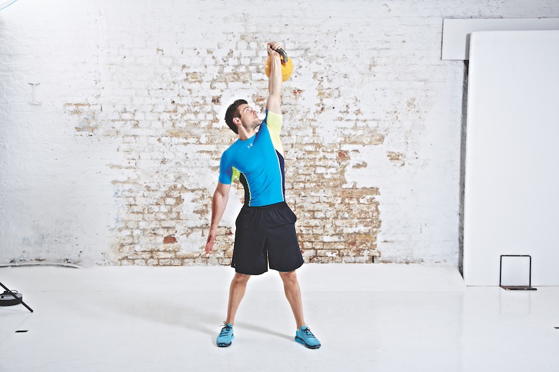 Man in blue top and black shorts performing kettlebell Turkish get-up