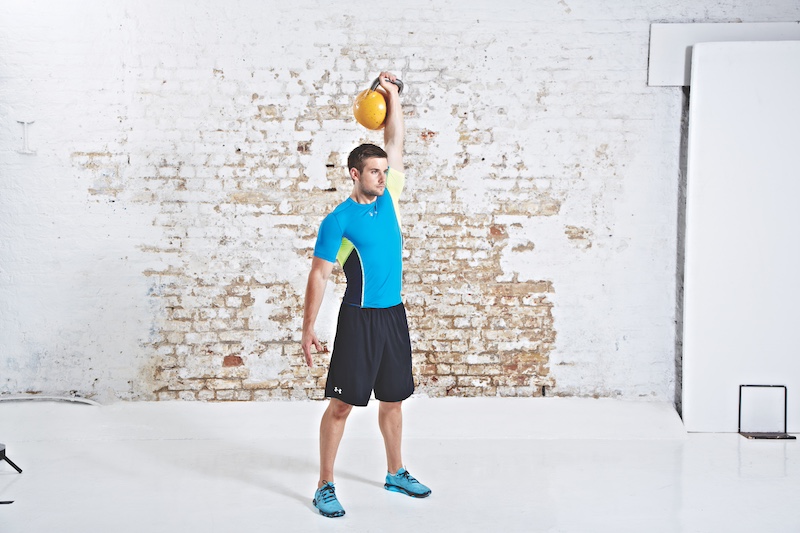 Man in blue top and black shorts performing kettlebell clean and press