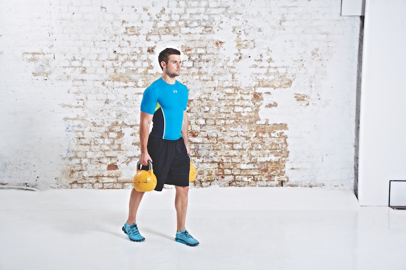 Man in blue top and black shorts performing kettlebell farmer's carry