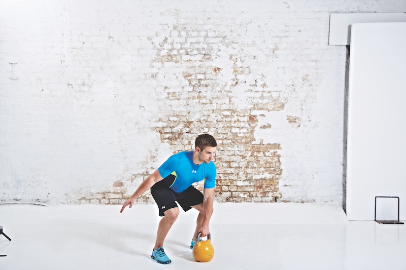 Man in blue top and black shorts performing kettlebell snatch