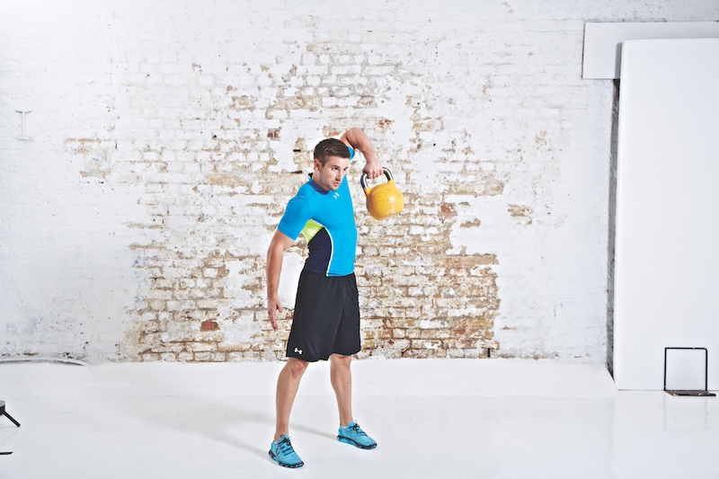 Man in blue top and black shorts performing kettlebell snatch