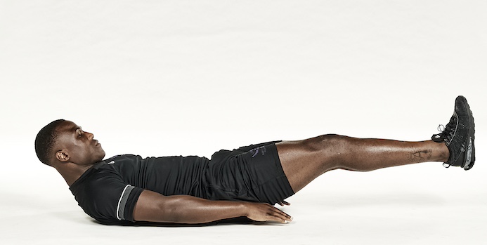 Man in black shorts and black training top performing lying leg raise