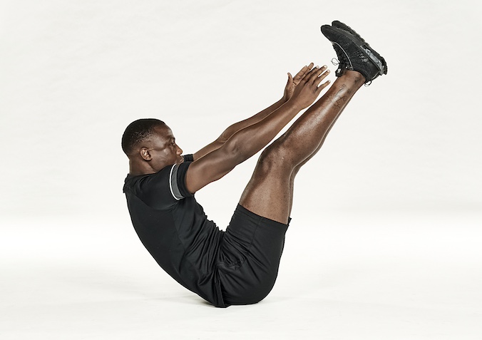 Man in black shorts and black training top performing V-sit abs exercise