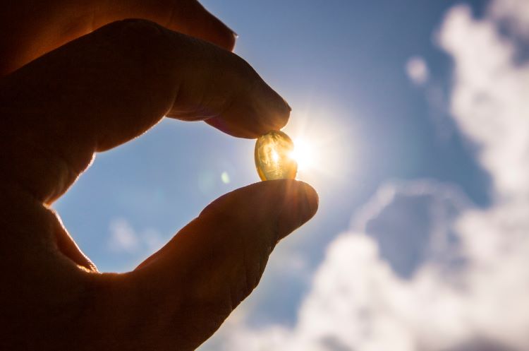 Silhouette of a man's hand holding a vitamin D tablet up to the sun