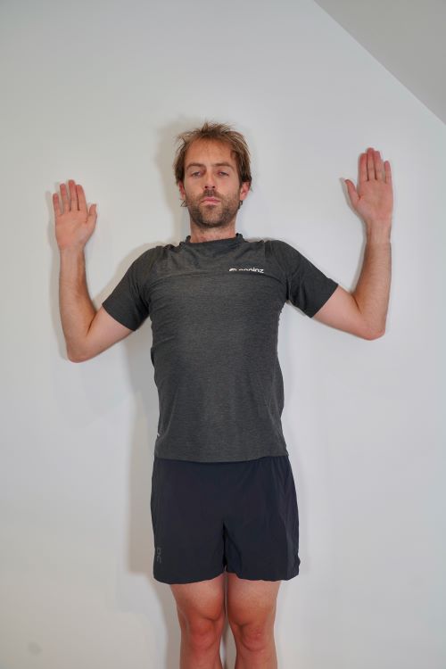 Man stretching arms and shoulders against a wall