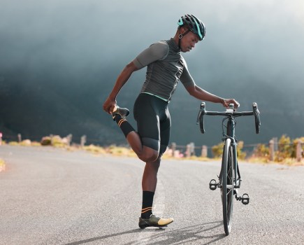 man stretching by his bike on a mountain road
