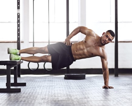 topless man in gym performing side plank on bench