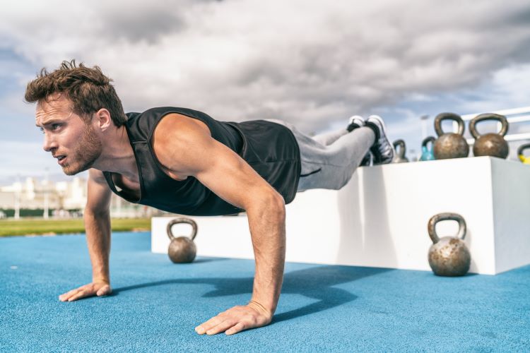 Man surrounded by weights performing decline press-up outdoors