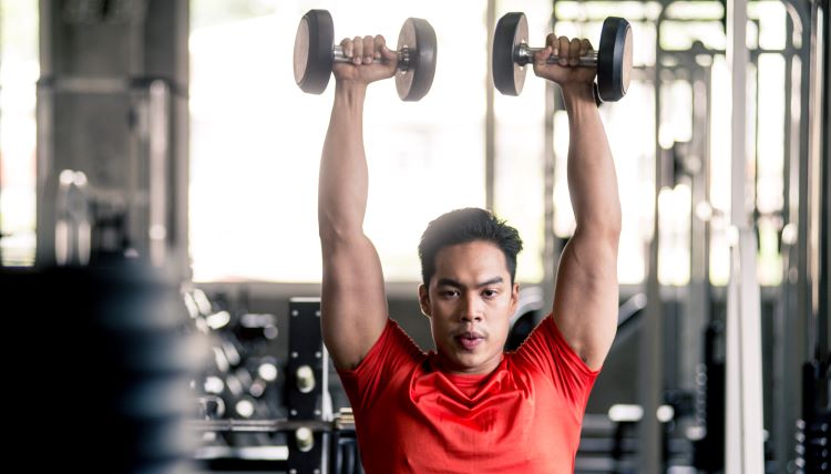 Man in a gym performing dumbbell shoulder presses