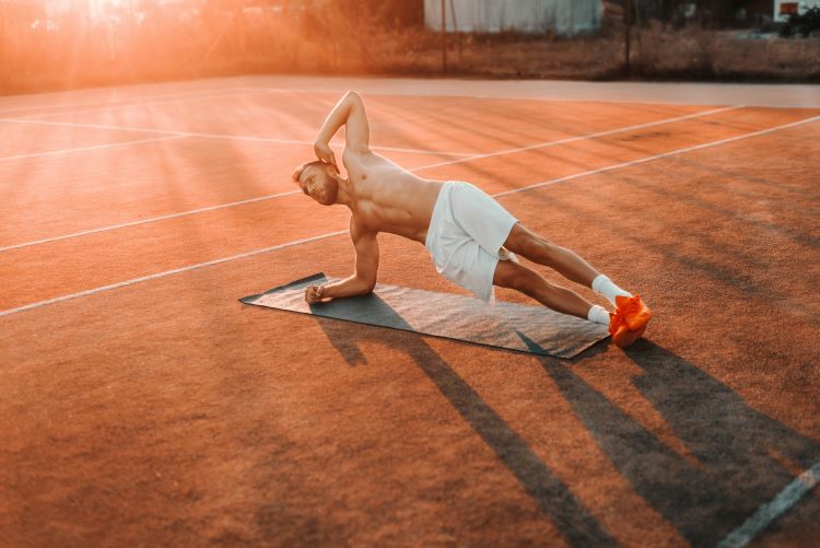 Man performing a side plank on a tennis court