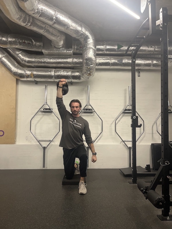 man performing half-kneeling kettlebell press in the gym