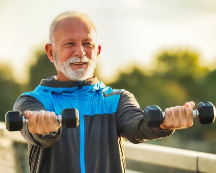 Elderly man exercising outside with pair of dumbbells