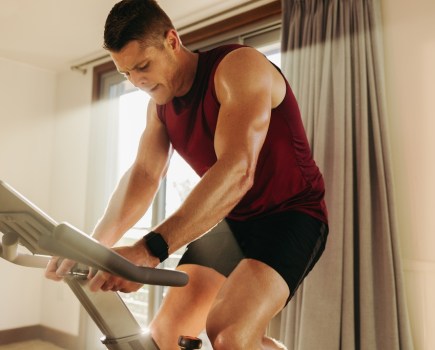 Male athlete using a smart exercise bike to boost his fitness, taking full advantage of fitness technology to stay on top of his game. Young Caucasian man crushing his cardio workout at home