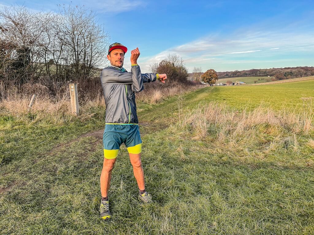 Running coach Simon James performing arms stretch in a field after a trail run