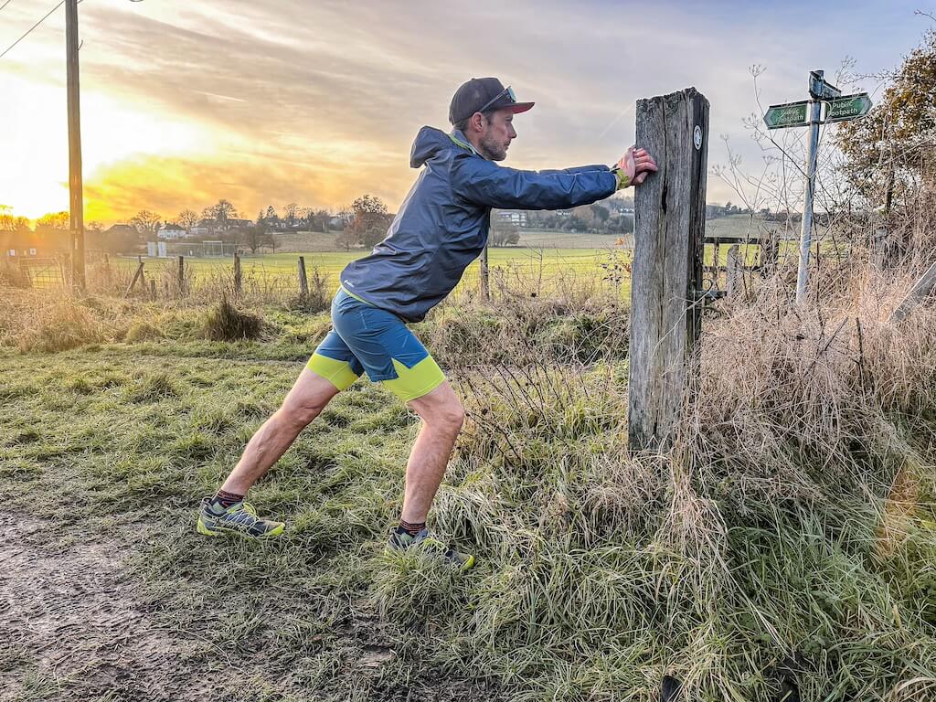 Running coach Simon James performing calf stretch in a field after a trail run