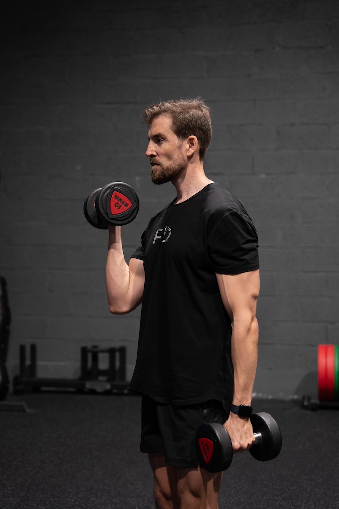 PT demonstrating how to perform a dumbbell single-arm curl in a workout routine for beginners