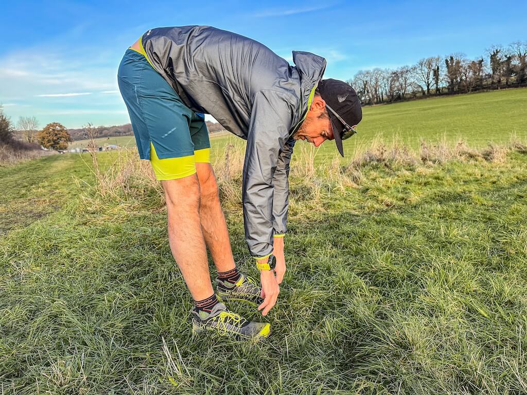 Running coach Simon James performing hang stretch in a field after a trail run