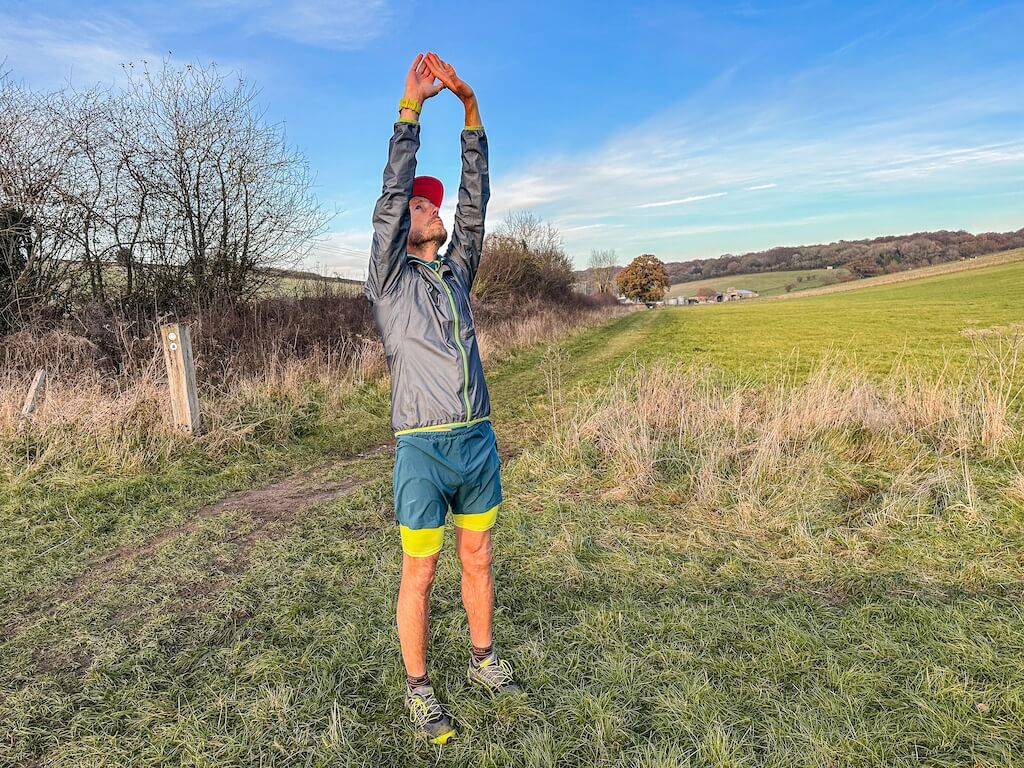 Running coach Simon James performing stretch in a field after a trail run