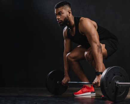 A man squatting to lift a barbell wearing red lifting shoes
