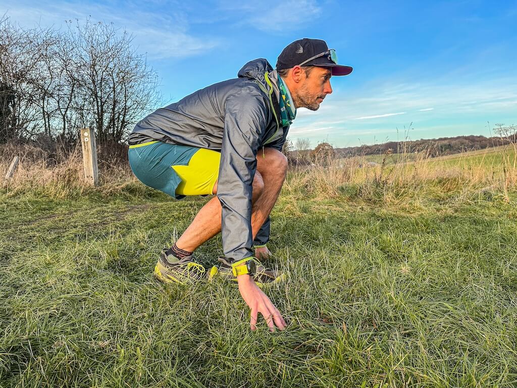 Running coach Simon James performing soleus stretch in a field after a trail run