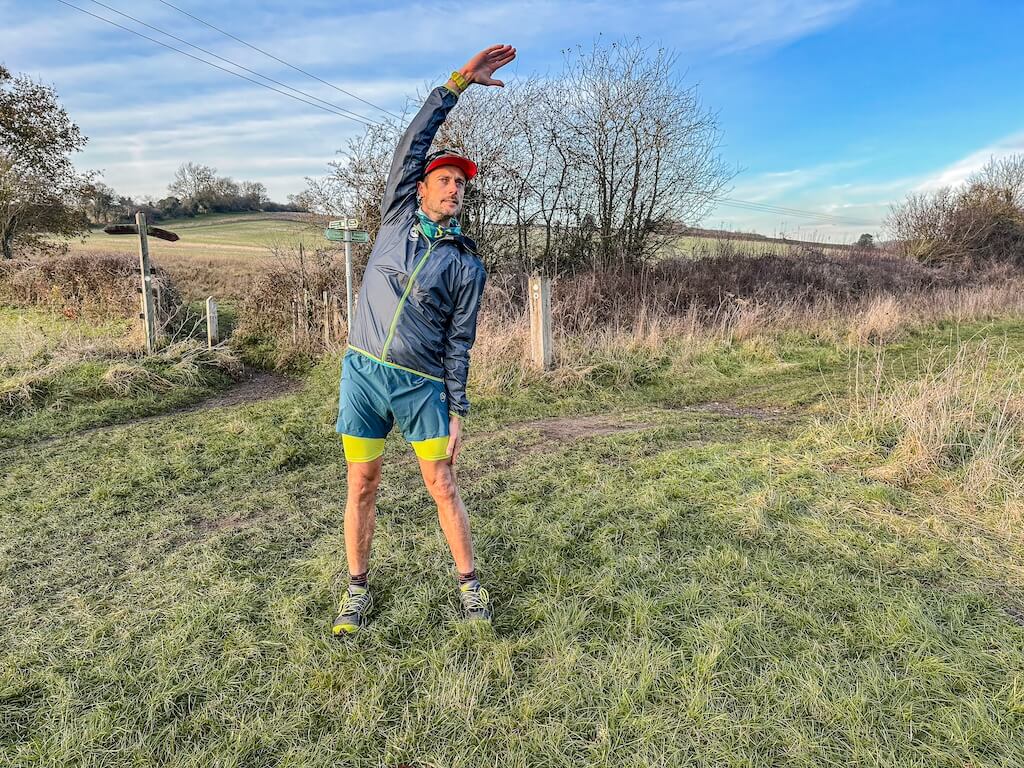 Running coach Simon James performing torso stretch in a field after a trail run