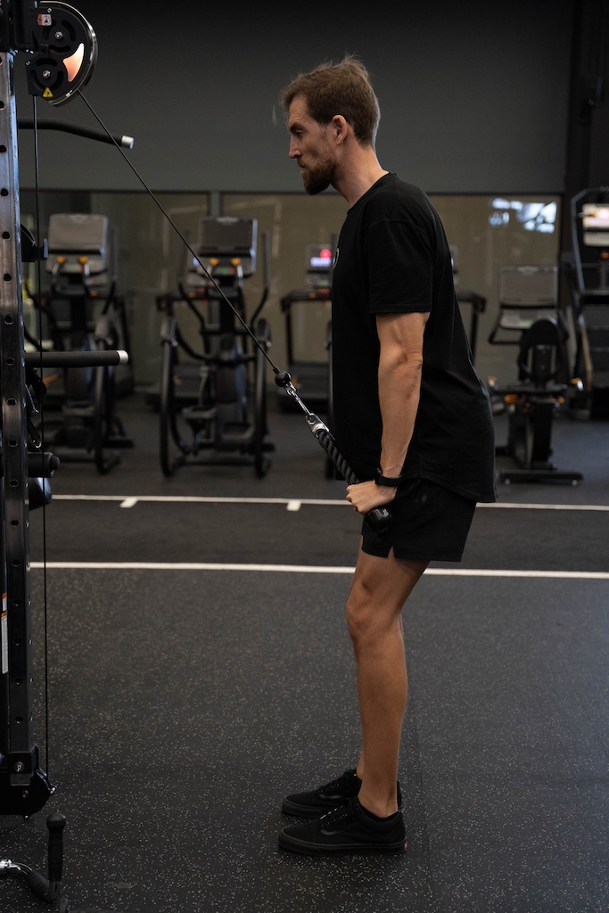 PT demonstrating how to perform a triceps rope pushdown in a workout routine for beginners