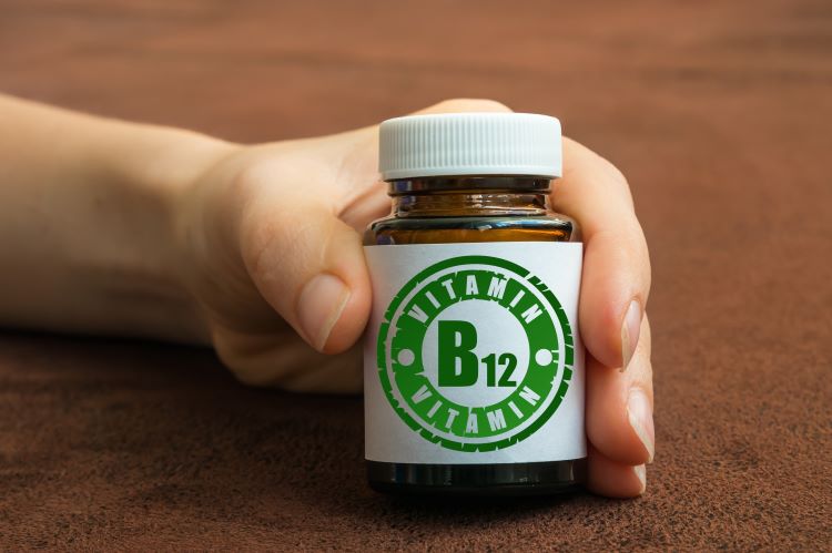 A hand holding a bottle of Vitamin B12 tablets