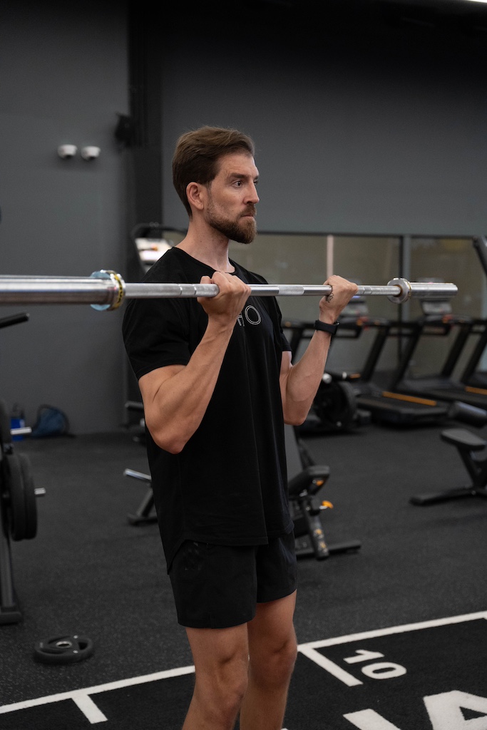 PT demonstrating how to perform a barbell curl in a workout routine for beginners