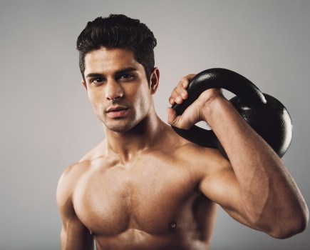 topless man holding kettlebell on one shoulder