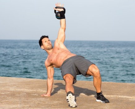 topless man exercising with kettlebell on the beach