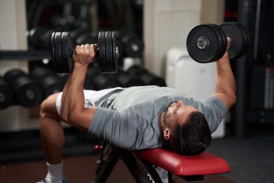 Young fitness man doing bench press with heavy dumbbells for chest workout