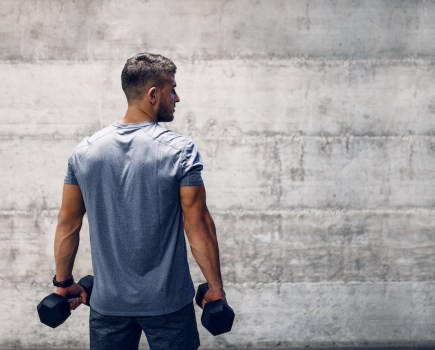 man with back to camera holding pair of dumbbells