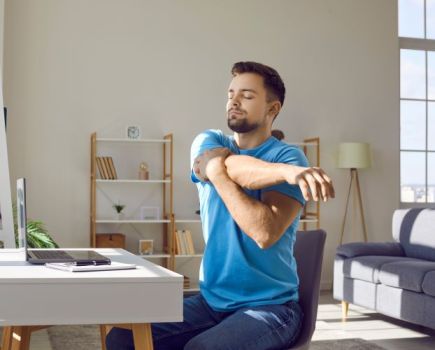 Man stretching shoulders at his desk