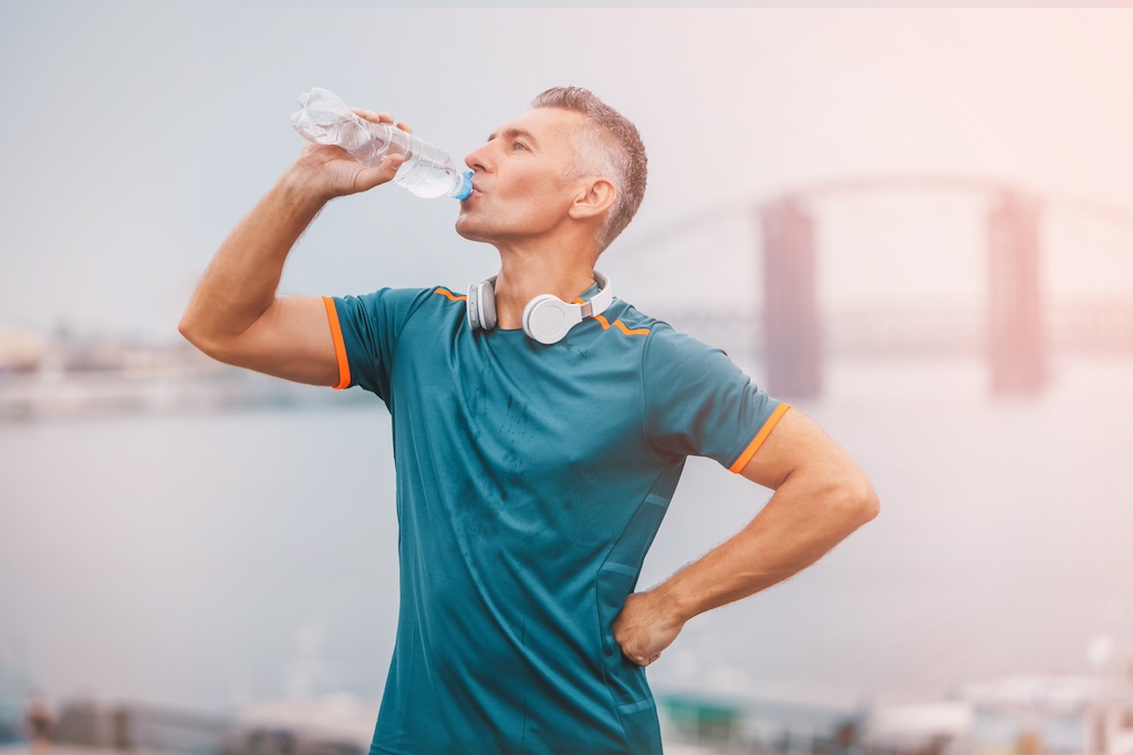 Portrait of healthy athletic middle aged man with fit body holding bottle of refreshing water, resting after workout or running. middle aged male with a drink after outdoor training