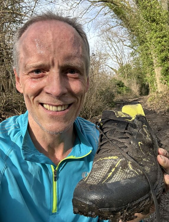 Close-up of a man in the woods holding up a running shoe