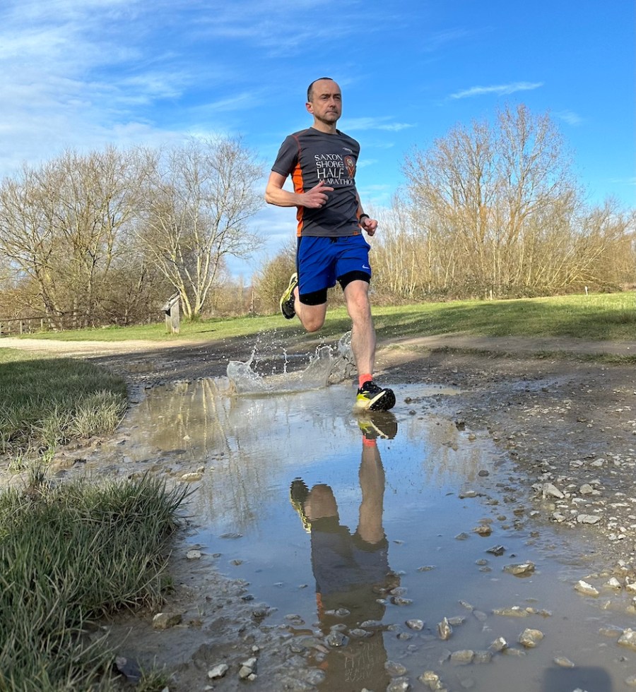 trail runner splashes through puddle while testing a pair of the Salomon S/Lab Genesis running shoes