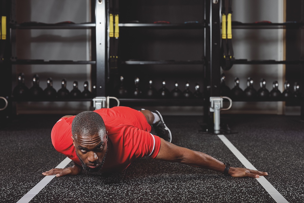 man in red top and red shorts doing a typewriter push-up in the gym as part of a full-body circuit