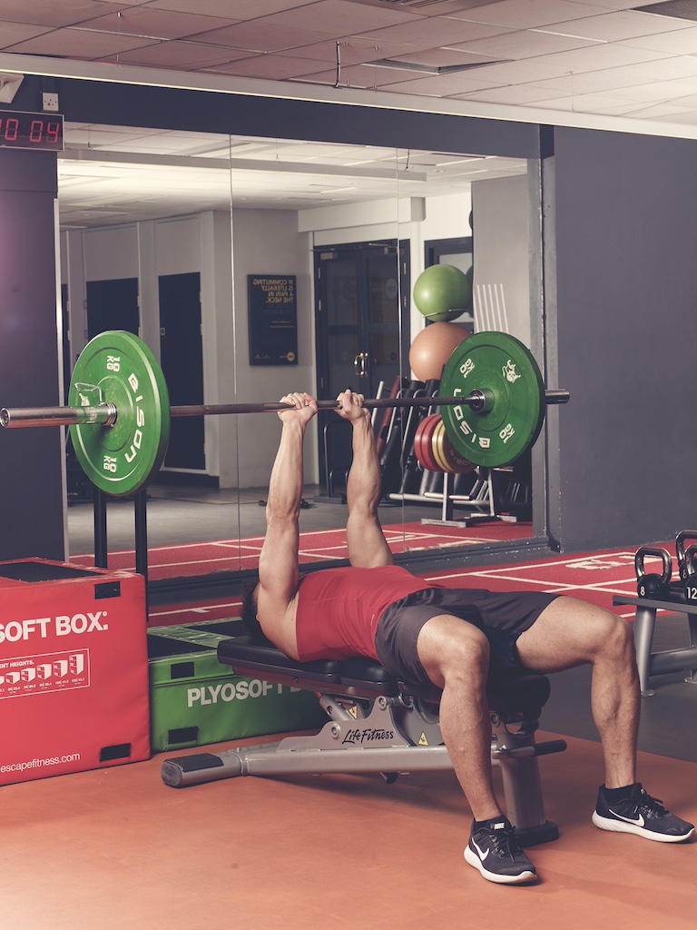 man in red vest and black shorts performing close-grip bench press in the gym