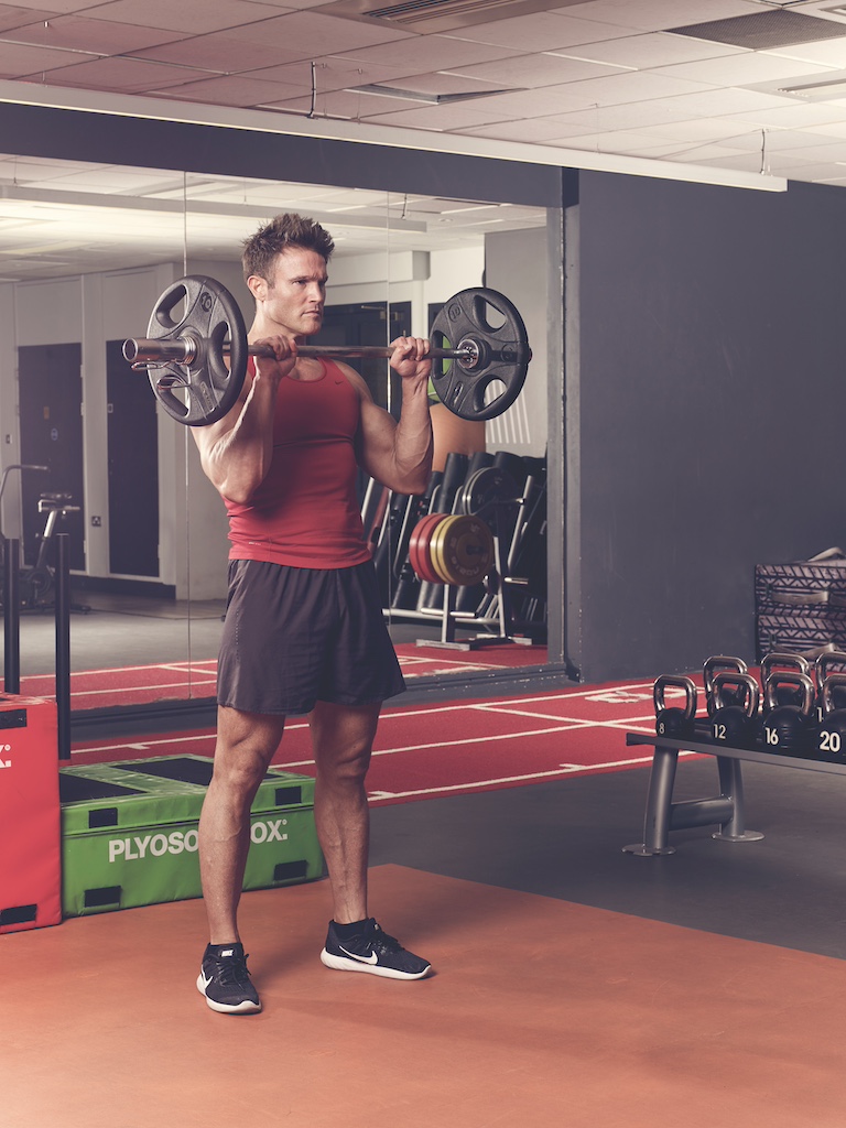 man in red vest and black shorts performing EZ-bar reverse curl in the gym – one of the best barbell arms exercises