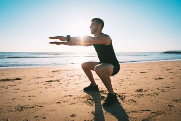 Man on a beach performing a bodyweight squat