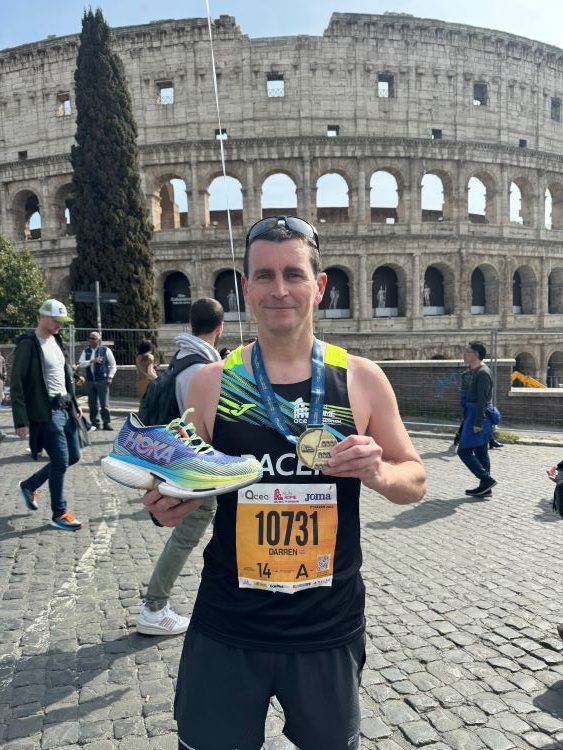 Runner holding a shoe and a medal outside Rome Colosseum