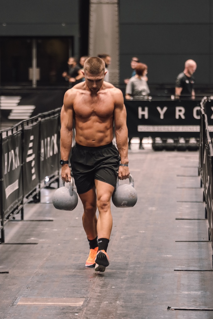 Jake Dearden performing kettlebell farmer's carries during a HYROX event