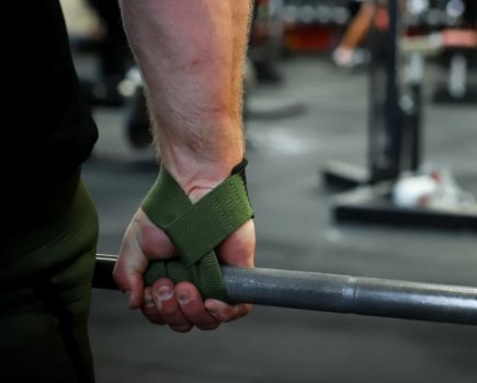Close-up of a man's hand, using lifting straps with a barbell