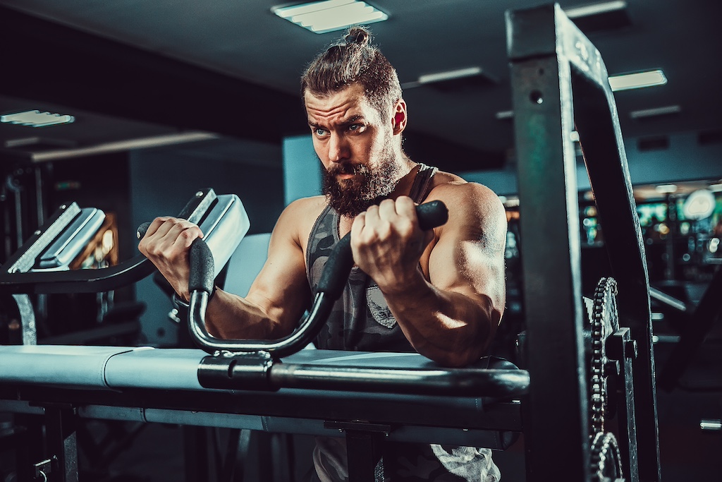 bearded man in vest performing bicep exercise in the gym
